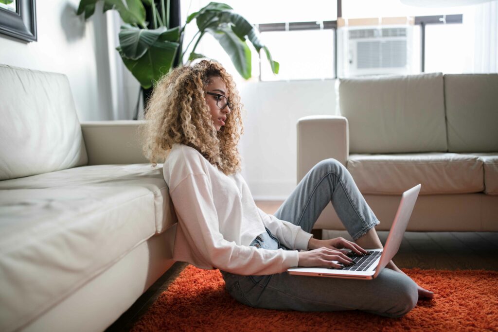 Copywriting vs Content Writing blog post image featuring a woman with blond curly hair sitting on the floor and working on a laptop