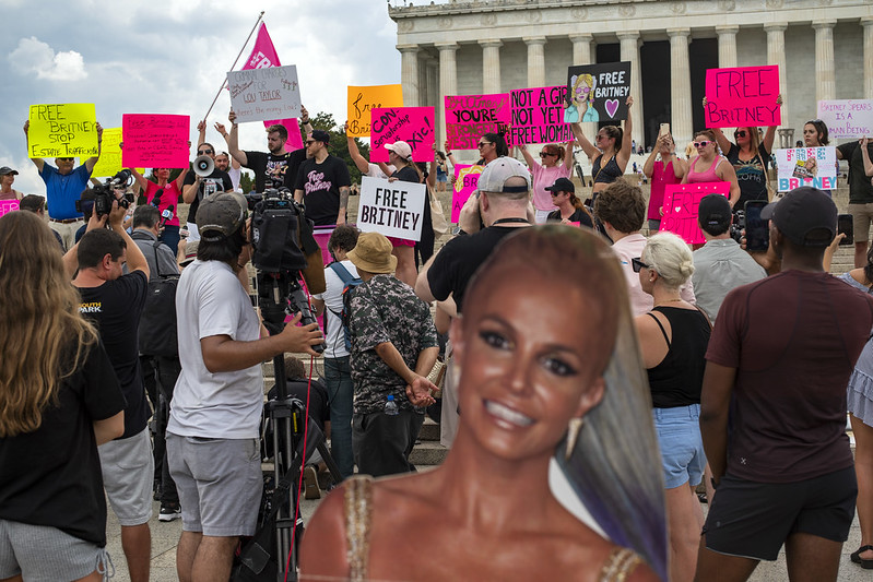 A crowd of Britney Spears supporters hold up signs for the media in front of the Lincoln Memorial. A cardboard Britney is in the foreground