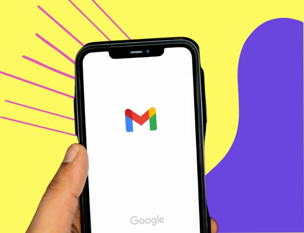hand holding a phone with the gmail logo in front of swirling background for post about creating newsletters