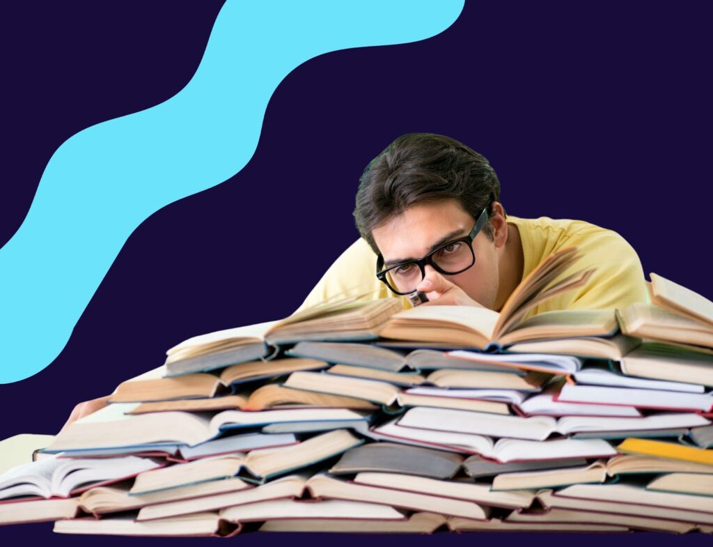 Exhausted man in glasses looking over piles of books in front of blue background