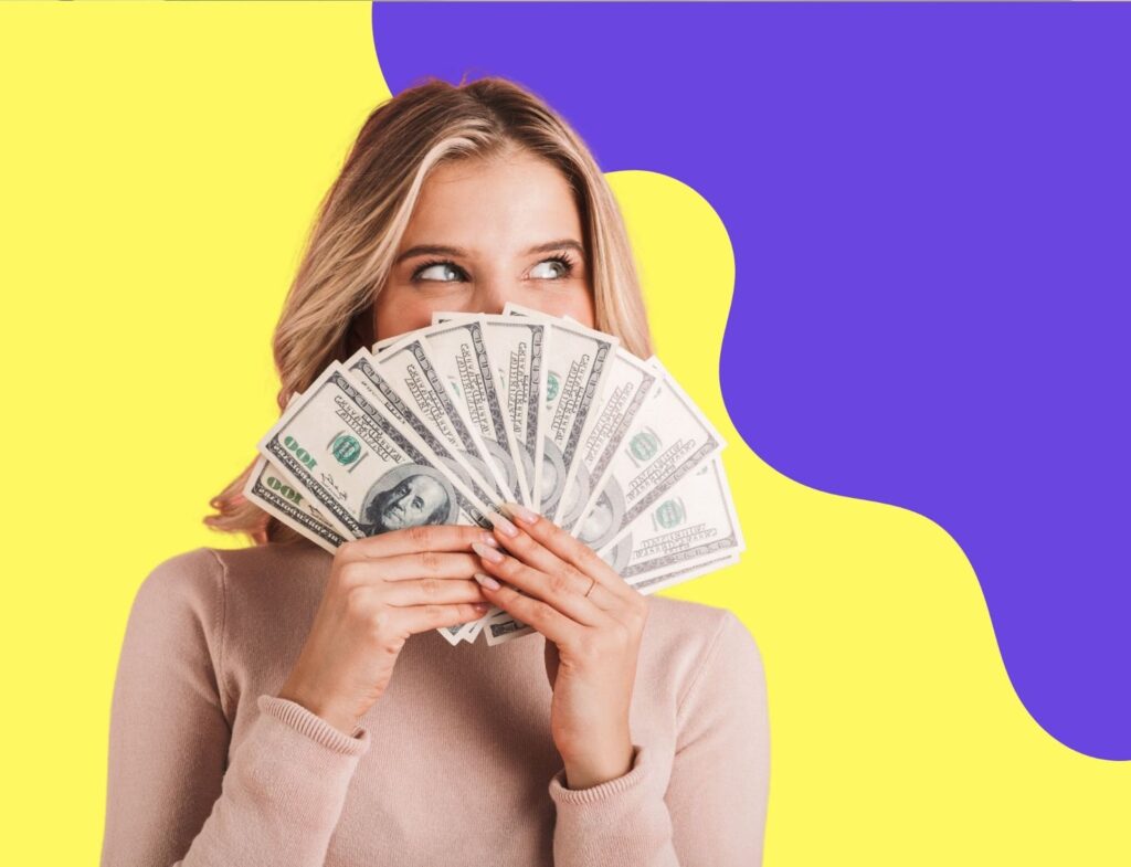 blonde woman fanning cash in front of her face and looking happy to the side in front of blue and yellow abstract background