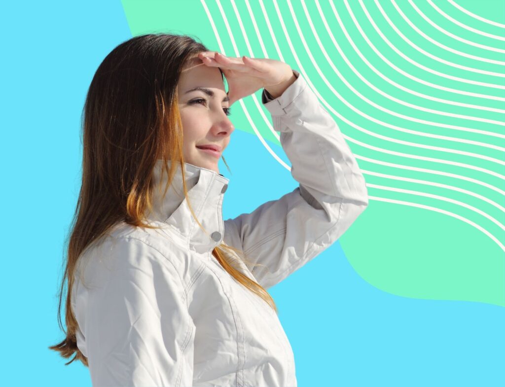 Woman in white windbreaker jacket smiling with hand over her eyes looking toward the future with pastel green and blue background