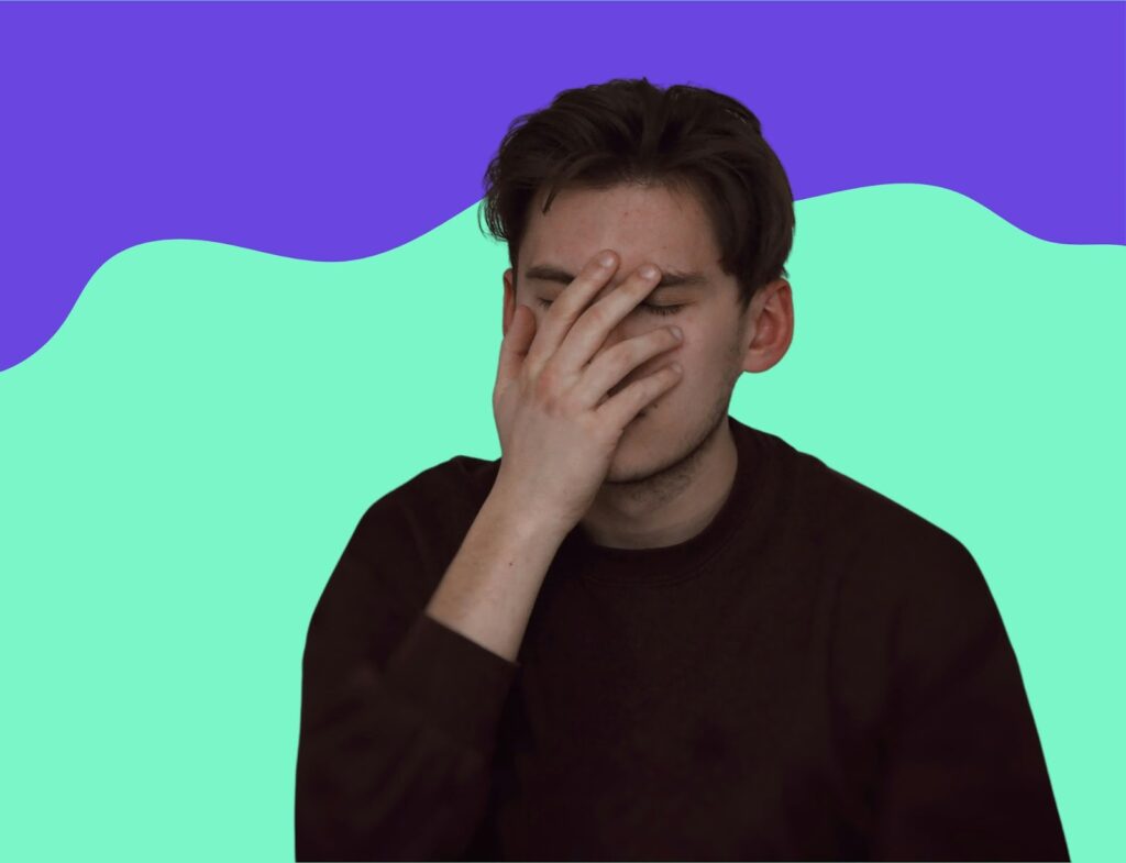 Man in black crewneck sweater putting his hand to his face in annoyance in front of blue and green background