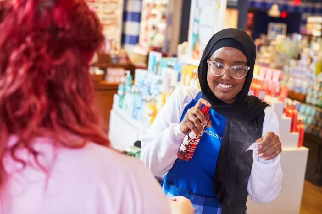 Bath and Body Works employee spraying body splash on a tester sheet for a customer in one of their retail stores